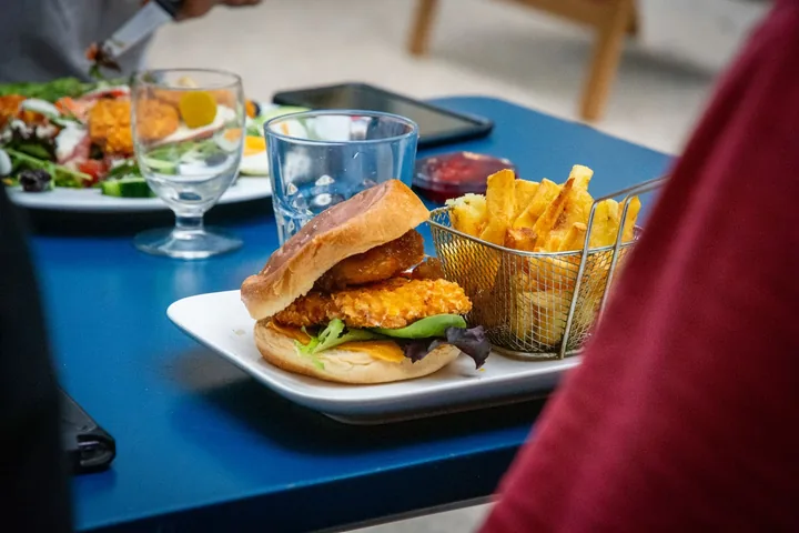 Burger au poulet pané et frites dans un panier, sur une table bleue
