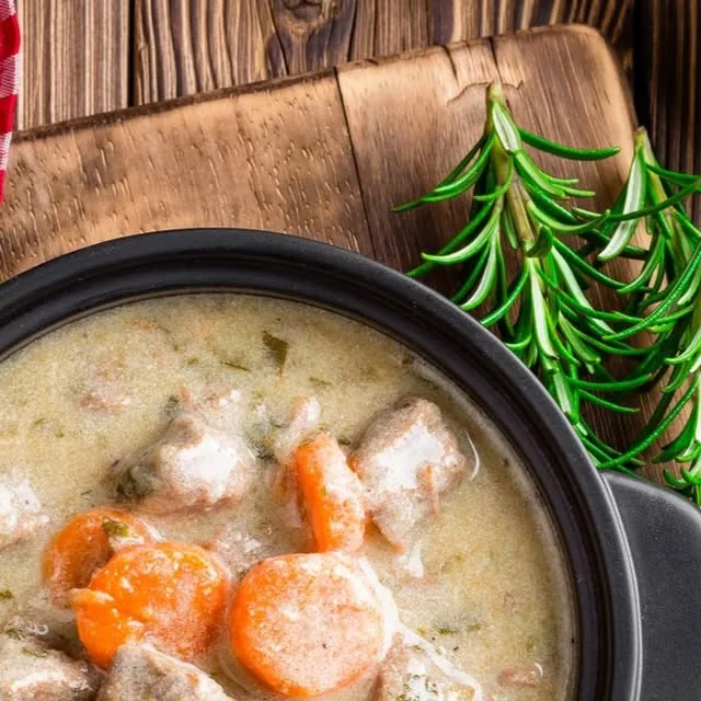 Plat mijoté en cocotte : morceaux de viande, carottes et sauce crémeuse, avec une branche de romarin