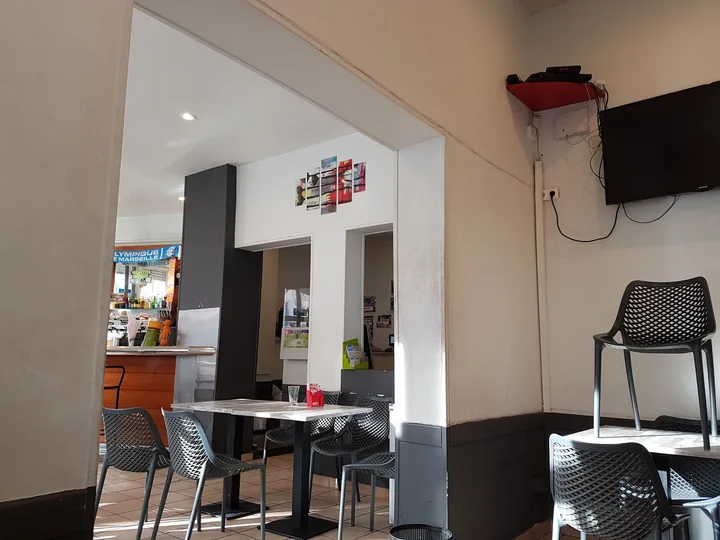 La salle : tables hautes, chaises grises ajourées, comptoir et télévision au fond